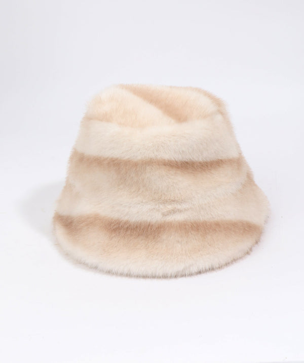 A fuzzy faux fur bucket hat in a soft beige and cream color-blocked pattern, photographed on a seamless white background.