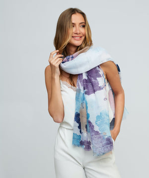Blue oblong scarf featuring a soft abstract watercolour print in blue, purple, white, and beige tones for a refined seasonal look. Crafted from lightweight, semi-sheer fabric with frayed edges for a relaxed, modern finish. Suitable for versatile styling as a neck scarf, shawl, or wrap.