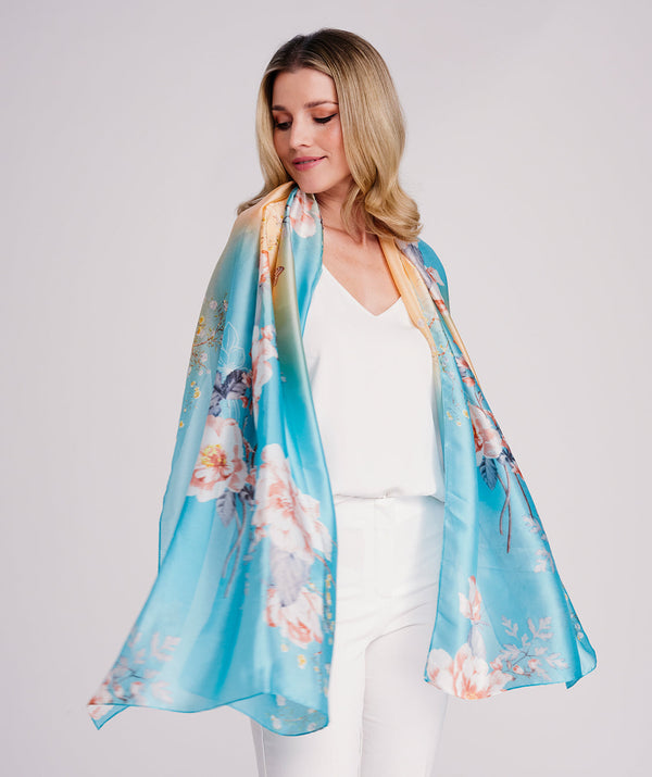 Blue oblong scarf featuring a delicate floral print in pale turquoise and soft cream tones for an elegant seasonal finish. Crafted from soft, lightweight satin silk with a smooth drape and polished hemline edging for a refined look. Suitable for versatile styling as a neck scarf, shawl, or wrap.